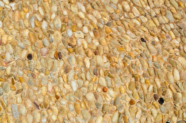 Textur einer Steinmauer aus kleinen runden und ovalen Steinen mit Sand und Nähten