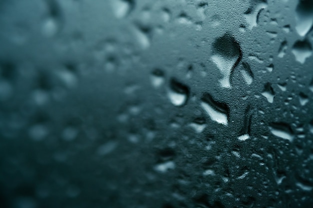 Textur von kleinen und großen Tropfen auf Glas vom Regen auf blauem Hintergrund