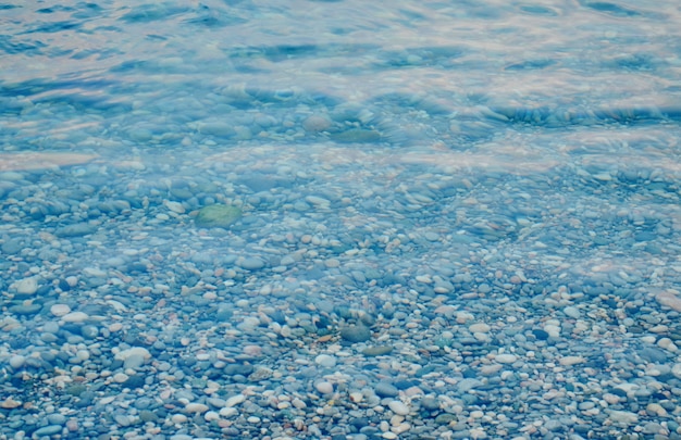 Textura de agua de mar cristalina transparente y guijarros, agua de mar de verano