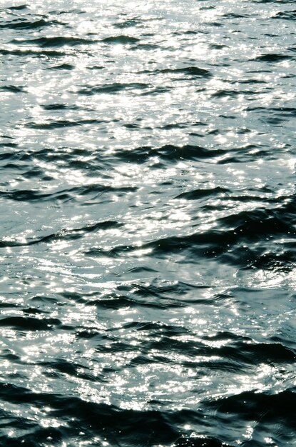 La textura del agua del río sundappled ondulada que refleja los rayos solares al atardecer hace que los perros de sol brillantes tonen azul