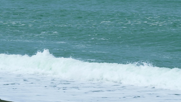 La textura azul pura y espumosa de la ola azul se eleva y choca con la orilla en tiempo real.