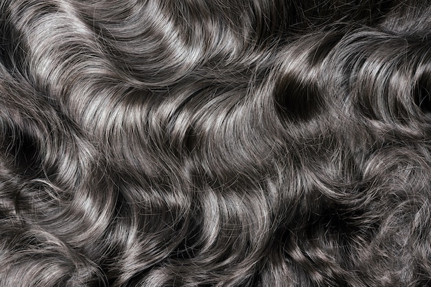 Textura de cabelo preto. Cabelo escuro longo cacheado ondulado feche como pano de fundo. Extensões de cabelo, materiais e cosméticos, cuidados com os cabelos. Penteado, corte de cabelo ou morte em salão.