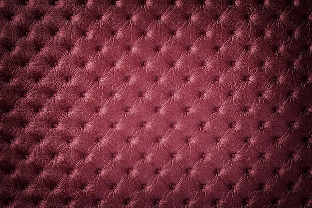 Textura de fundo de couro vermelho escuro com padrão de capitone, macro. Têxteis de vinho do estilo retro de Chesterfield. Cenário de tecido rubi vintage com vinheta.