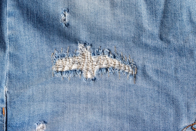 Textura de tecido de jeans rasgado. jeans envelhecidos com orifício costurado e fundo de costura