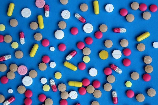 Textura de diversas drogas y píldoras esparcidas sobre una pared azul. Pastillas brillantes y multicolores. Tema de salud y medicina.