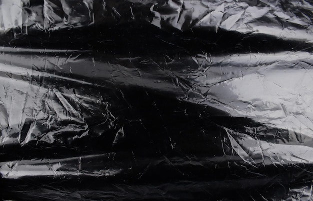 Foto textura de envoltura de plástico arrugado sobre un fondo negro papel tapiz de paquete de celofán
