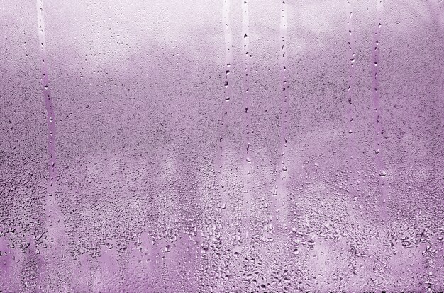 Textura de una gota de la lluvia en un fondo transparente mojado de cristal. Tonos en color rosa.