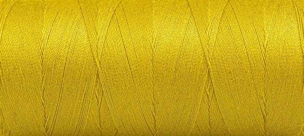Textura de hilos en un carrete de color amarillo sobre un fondo blanco.