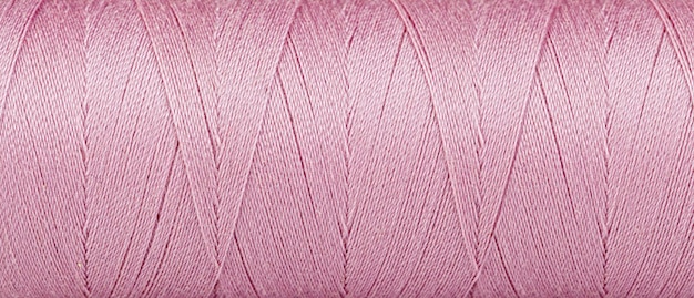 Textura de hilos en un carrete de color rosa sobre un fondo blanco.