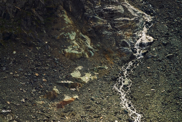 Textura natural detalhada da inclinação de pedras soltas. O córrego da água da montanha flui para baixo da montanha. Pequena cachoeira na rocha. Paisagem incomum de natureza majestosa.