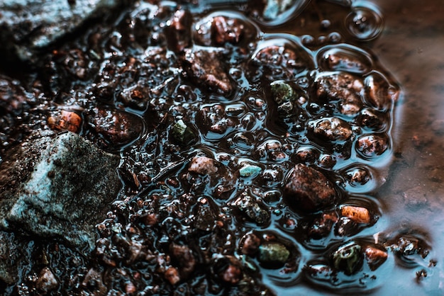 Textura de pequeñas piedras en un charco de agua luz solar natural viejo asfalto arruinado El fondo es muy detallado