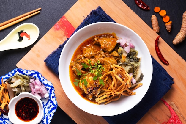 Foto thai-food-konzept khao soi oder khao soja thai-curry-rindfleisch mit eiernudeln auf holzbrett auf schwarzem hintergrund mit kopierraum