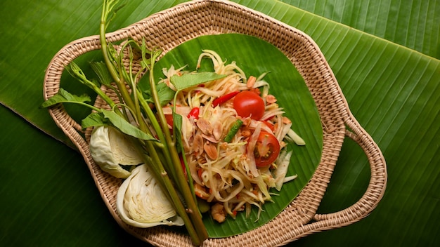 Thai-Food-Papaya-Salat Somtum mit Gemüse auf Weidentablett auf Bananenblättern-Hintergrund