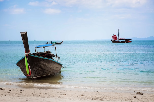 Thai-Longtail-Boot am Strand von Phra Nang vor Anker im Sandhintergrund eines schwarzen Segelschiffs