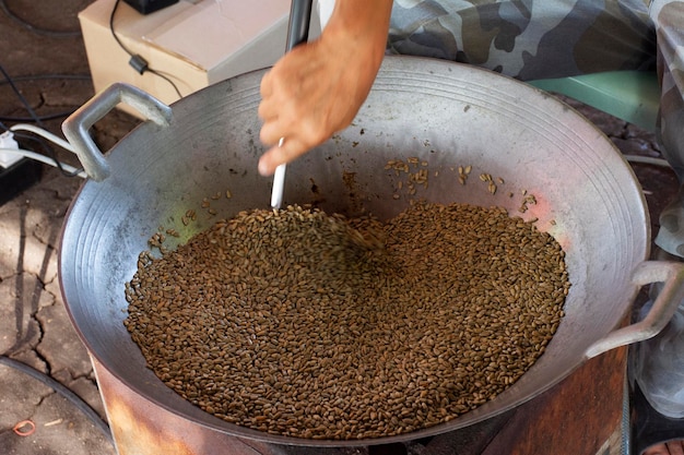 Thailänder kochen lokale Speisen geröstete Sonnenblumen Samen Getreide mit Honig und Salz in Stahlpfanne auf Gasofen für Kunden Reisende wählen leckere kaufen und essen im Straßenmarkt Bazar in Lopburi Thailand