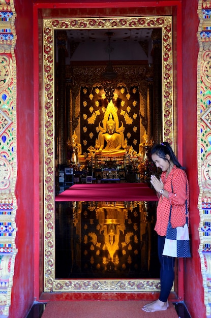 Thailändische Frau betet mit Reflektion Goldene Buddha-Statue in der Kirche Wat Phra That Suthon Mongkhon Khiri in Phrae Thailand