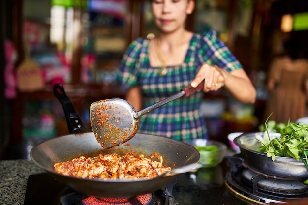 Thailändische Frau, die rotes würziges Hühnercurry im Wok kocht