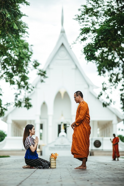 Thailändische Frau mit traditionellem Kleid, das mit Mönch betet