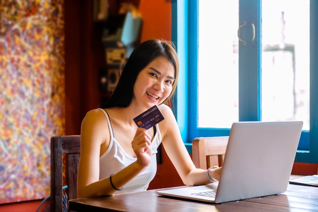 Thailändische Frau trinkt Orangensaft in einem Café Mit Laptop online einkaufen Arbeiten Sie mit einem Computer in einem Café