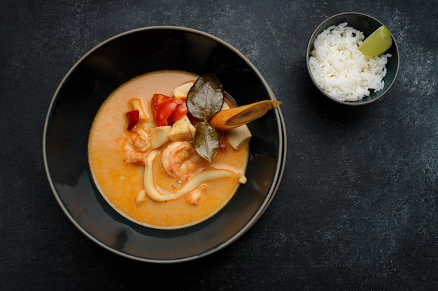 Thailändische Suppe mit Meeresfrüchten und Reis auf dunklem Beton