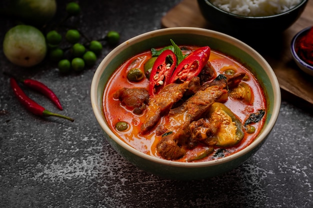 Thailändisches Essen - würziges rotes Schweinefleisch-Curry mit Zutaten auf dunklem Tisch