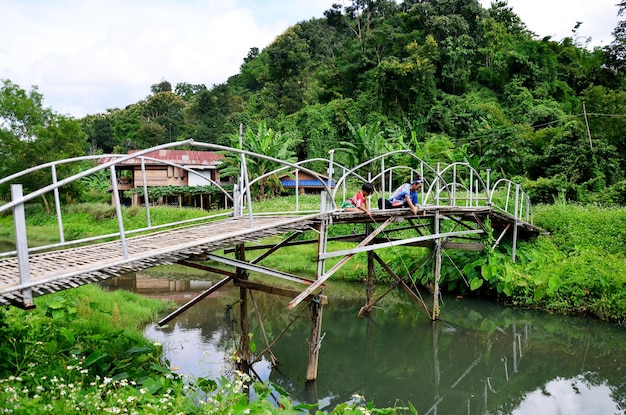 Thailändisches Frauenporträt mit Kindern, die am 30. August 2015 in Phrae Thailand auf der Bambusbrücke im Dorf Baan Natong fischen