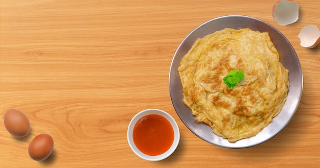 Foto thailändisches omelett mit chilisauce auf holztisch