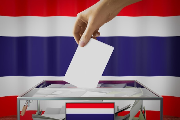 Thailand-Flaggen-Hand, die Wahlkarte in ein Kastenwahl-Wahlkonzept fallen lässt