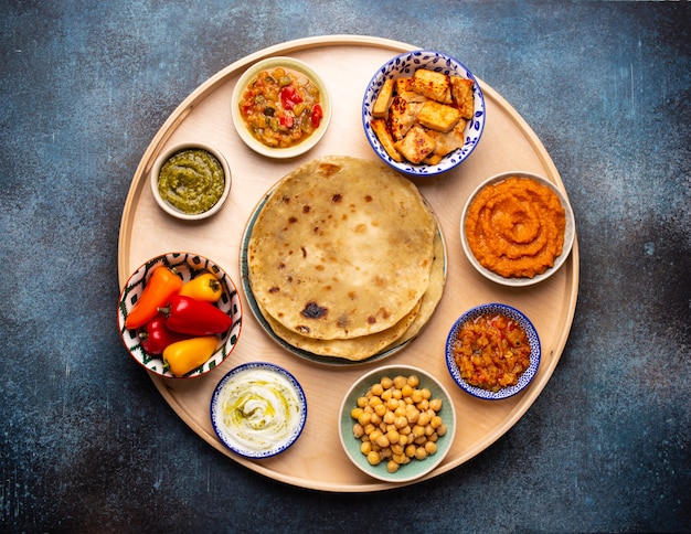 Thali indio: selección de varios platos servidos en bandeja de madera redonda. Meze vegetariano indio surtido con pan chapati tradicional, paneer, dal, chutney en diferentes tazones. Vista superior