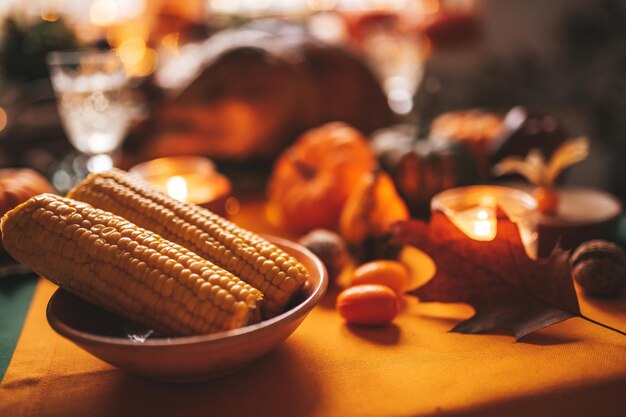 Thanksgiving-Abendessen mit festlicher Herbstdekoration und Kerzen. Esstisch für die ganze Familie mit köstlichem goldgebratenem Truthahn auf einer mit Rosmarin garnierten Platte und frischen kleinen Kürbissen