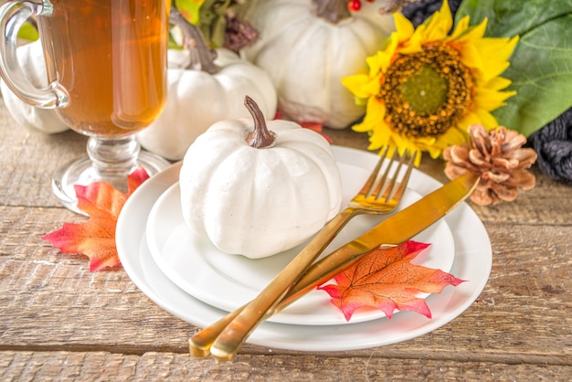 Thanksgiving-Food-Konzept. Herbsttischdekoration mit Teller, Teetasse, Kürbissen, Sonnenblumen und warmem Plaid oder Pullover, Komfort und gemütlichem Hintergrundkopierraum aus Backsteinholz