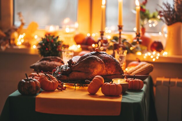 Thanksgiving-Tag-Abendessen mit Feiertag-Herbstdekorationen und Kerzen Familien-Esszimmer-Tisch mit köstlichem goldenen gerösteten Truthahn auf einem Teller, garniert mit Rosmarin, frischen kleinen Kürbissen