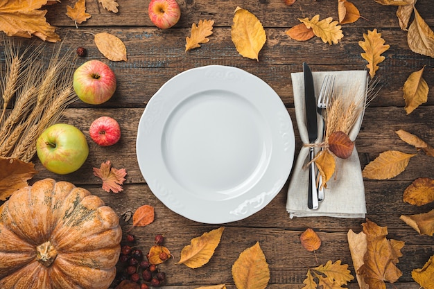 Thanksgiving-Tageshintergrund mit Besteckkürbis-Serviettenäpfeln und trockenen Blättern