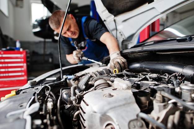 Thema Autoreparatur und -wartung. Mechaniker in Uniform, der im Autoservice arbeitet und den Motor überprüft.