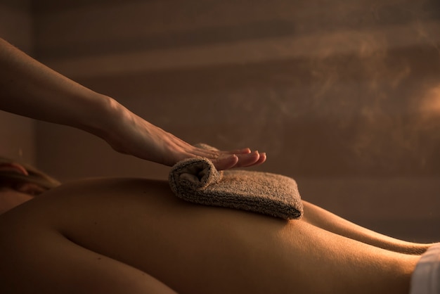 Therapeut, der die Rückseite der Frau mit heißem Tuch im Badekurort massiert