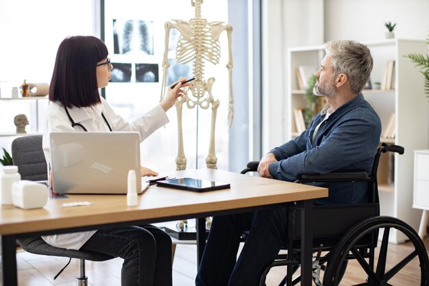 Foto therapeut verwendet skelett, um dem patienten die verletzte stelle zu zeigen