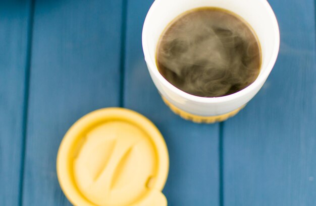 Thermobecher mit heißem Kaffee auf Holzhintergrund