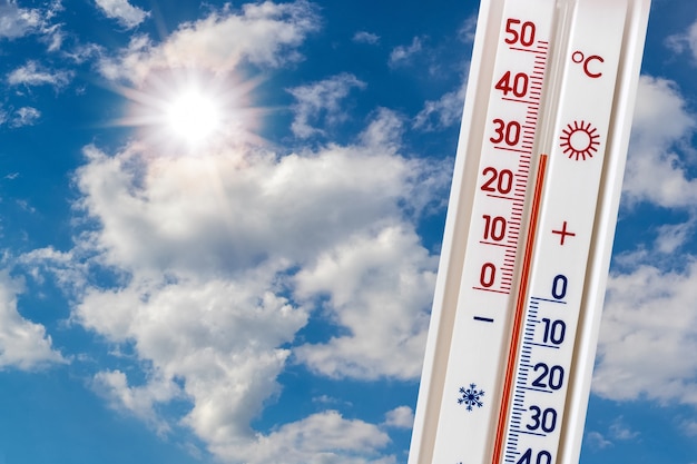 Thermometer auf blauem Himmel mit weißen Wolken und Sonne zeigt 30 Grad Hitze. Sommerhitze