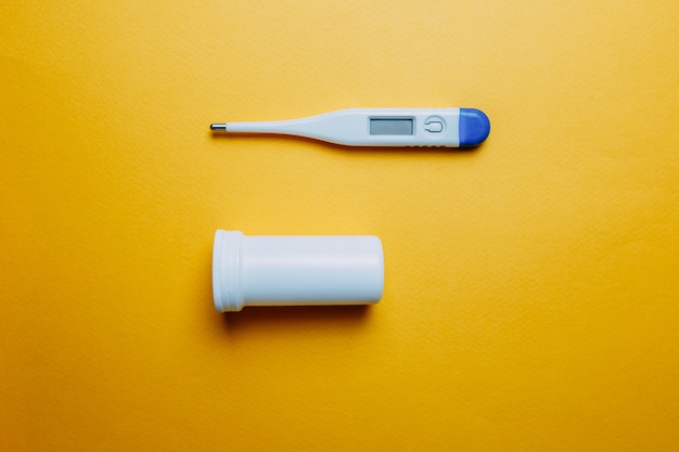 Thermometer mit hoher Temperatur und Pillen auf orange Hintergrund. Impfstoff gegen Coronavirus.