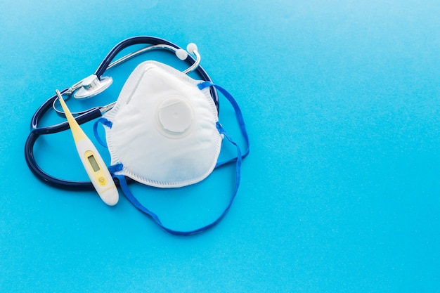 Thermometer, Stethoskop und Maske für Coronavirus-Schutz mit Copyspace auf blauem Hintergrund