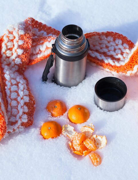 Foto thermos e mandarinas laranjas e lenço de tricô na neve