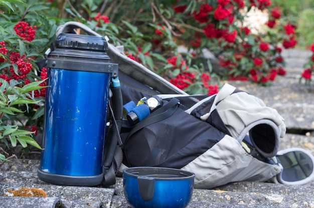 Thermos-Rucksack und Scheinwerfer Touristen-Ausrüstung Becher mit einem Getränk Fron-Ansicht