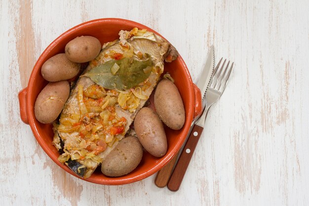 Thunfisch mit Zwiebel und Kartoffel im keramischen Teller auf weißer Holzoberfläche