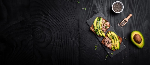 Thunfisch-Sandwiches mit Avocado und Microgreen auf Vollkornbrot-Holzhintergrund Leckere Thunfisch-Sandwiches zum Frühstück Gesunder Snack Draufsicht flach gelegt