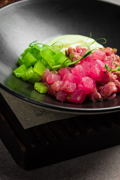 Thunfisch-Tartar mit eingelegter Gurke und Soße auf schwarzem Teller