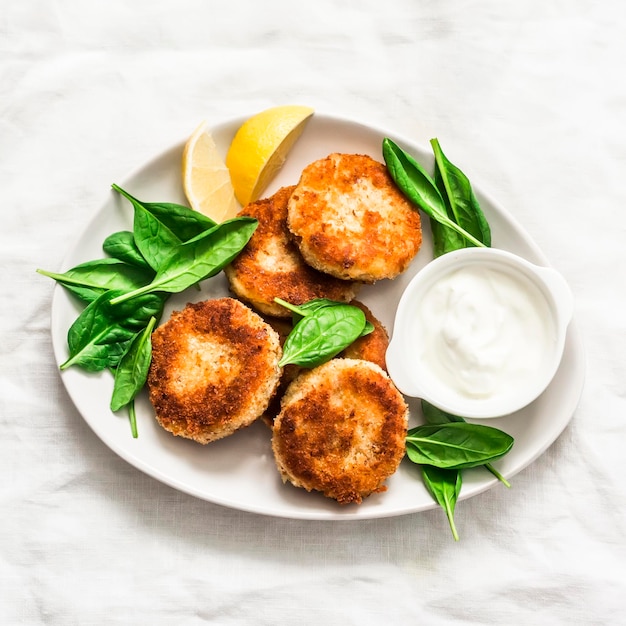 Thunfisch- und Kartoffelpastetchen, serviert mit Spinat und griechischem Joghurt auf hellem Hintergrund, Draufsicht