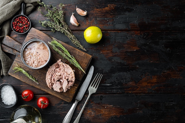 Thunfischkonserven, Fischkonserven, auf Holzschneidebrett, auf altem dunklem Holztisch mit Kräutern und Zutaten, Draufsicht flach gelegt