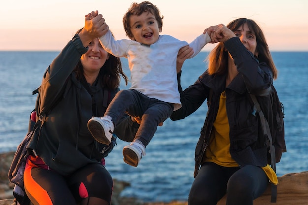 Foto tia caucasiana da criança e da mãe brincando com ele na costa à beira-mar ao pôr do sol