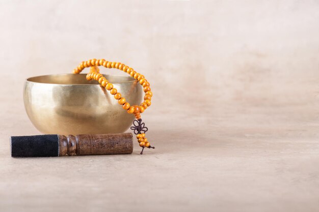 Tibetische Klangschale mit Stick-Mala-Perlensträngen, die bei Mantra-Meditationen auf beigem Steinhintergrund verwendet werden