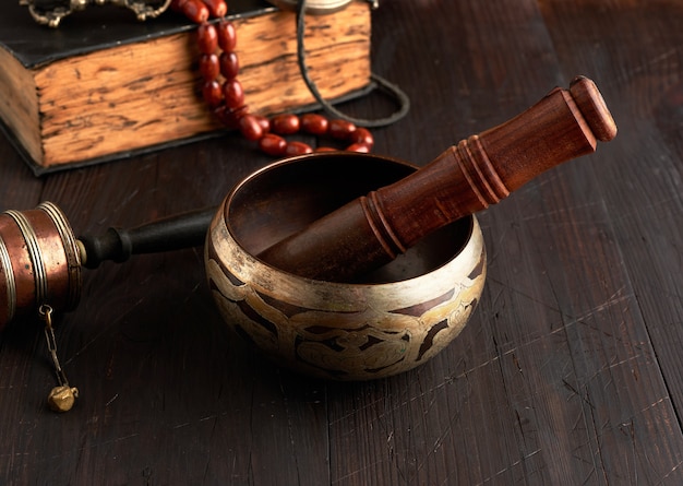 Tibetische singende Kupferschale mit einem hölzernen Klöppel auf einem braunen Holztisch